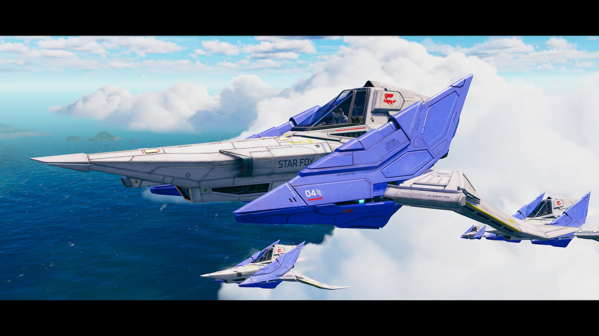 Capture de jeu montrant quatre chasseurs Arwing de Star Fox volant en formation au-dessus de l’océan et des nuages. L’appareil au premier plan, blanc et bleu, porte l’inscription « STAR FOX » sur le fuselage et le numéro 04 sur l’aile, tandis que les trois autres appareils suivent en arrière-plan sous un ciel dégagé.