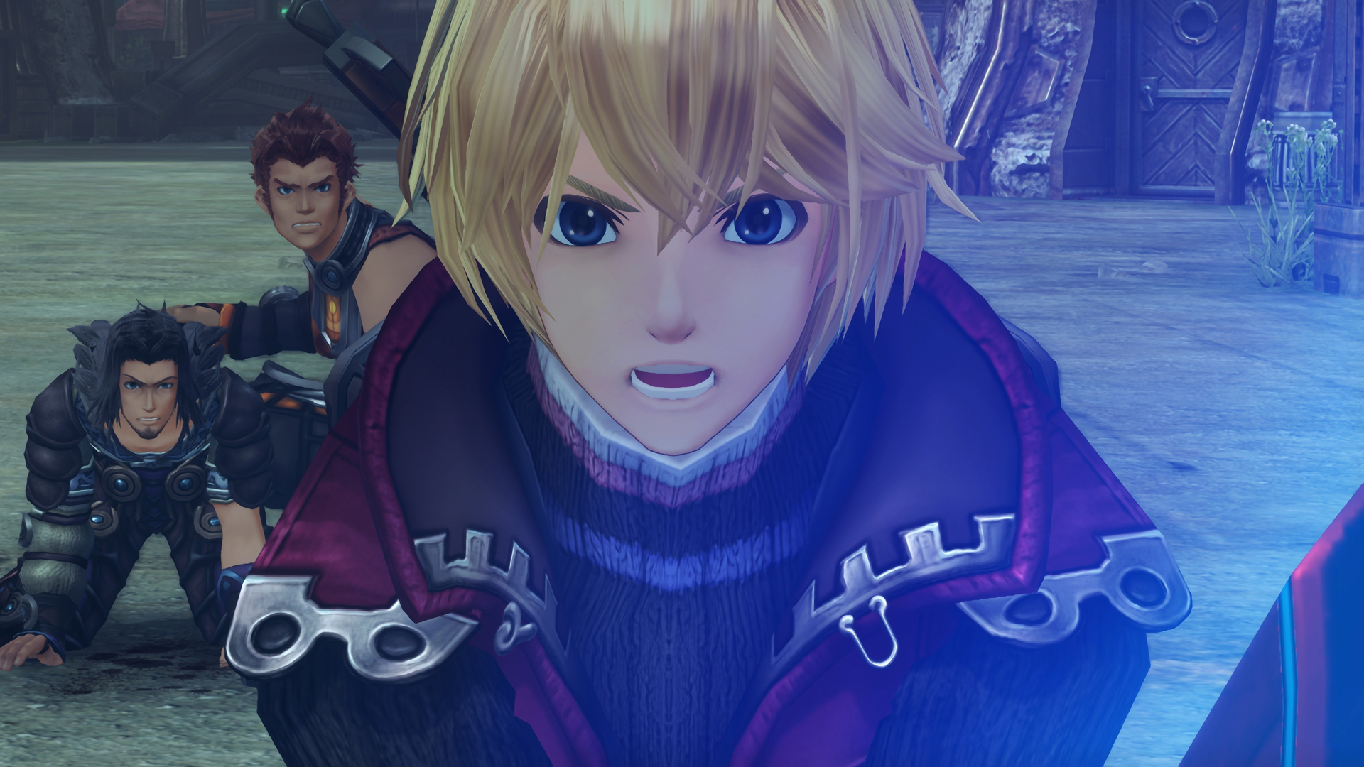 Capture d’écran de Xenoblade Chronicles: Definitive Edition montrant Shulk en gros plan, le visage tendu et éclairé par une lueur bleue. Derrière lui, deux compagnons se relèvent dans un décor de pierre et de métal, renforçant l’intensité dramatique d’une scène cinématique.