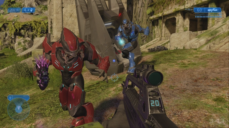 Capture d’écran dynamique du jeu Halo 2: Anniversary, montrant une scène de combat en vue à la première personne. Au centre, deux Élites — des ennemis extraterrestres emblématiques de la franchise Halo — foncent vers le joueur. L’un est équipé d’une armure rouge et brandit une arme à énergie violette, tandis que l’autre, en armure bleue, prépare une attaque avec une arme énergétique brillante. Leur apparence reptilienne, leurs mandibules proéminentes et leur stature imposante renforcent leur aspect redoutable. Au premier plan, on voit le fusil d’assaut du joueur, affichant un compteur de munitions numérique "20" sur le côté, typique de l’interface HUD du jeu. L’environnement est un mélange de nature luxuriante et de ruines technologiques forerunners : végétation verte, pierres anciennes et architecture futuriste grise en arrière-plan. L’interface affiche également une mini-carte circulaire en bas à gauche et une jauge de munitions bleue en haut à droite, illustrant le style iconique de Halo. Cette scène capture l’intensité des affrontements multijoueur ou de campagne, mêlant science-fiction, stratégie et réflexes dans un univers de guerre interstellaire.