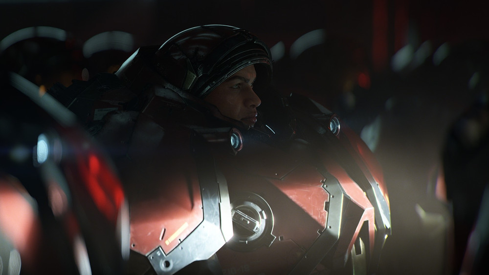 Capture d’une cinématique de science-fiction montrant un soldat en armure futuriste massive rouge et noire, casque ouvert laissant apparaître son visage. Il regarde sur le côté dans un environnement sombre, entouré d’autres silhouettes en armure.