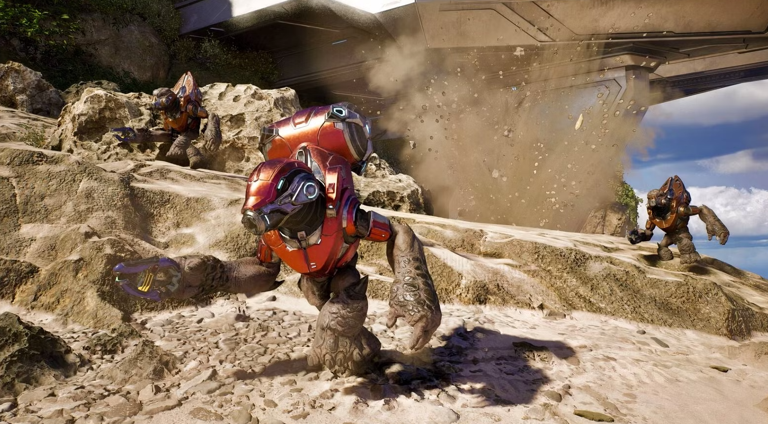 Capture de Halo montrant trois extraterrestres en armure rouge courant sur un terrain rocheux. Une explosion soulève poussière et débris près d’une imposante structure futuriste en arrière-plan.