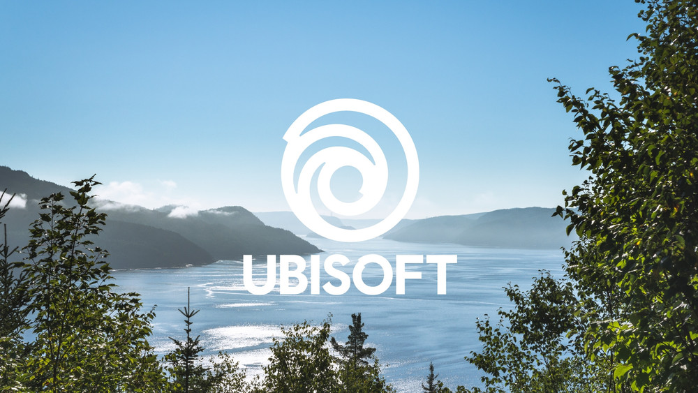 Visuel promotionnel montrant le logo blanc d’Ubisoft centré sur un paysage naturel composé d’un vaste plan d’eau entouré de montagnes boisées sous un ciel bleu. Des arbres encadrent l’image au premier plan, tandis que la lumière se reflète sur l’eau, créant une ambiance calme et lumineuse.
