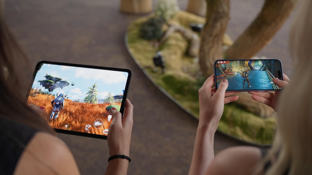 Deux personnes jouent à des jeux vidéo sur appareils mobiles, l’une sur une tablette montrant un personnage explorant un paysage coloré, l’autre sur un smartphone affichant une scène d’action futuriste.