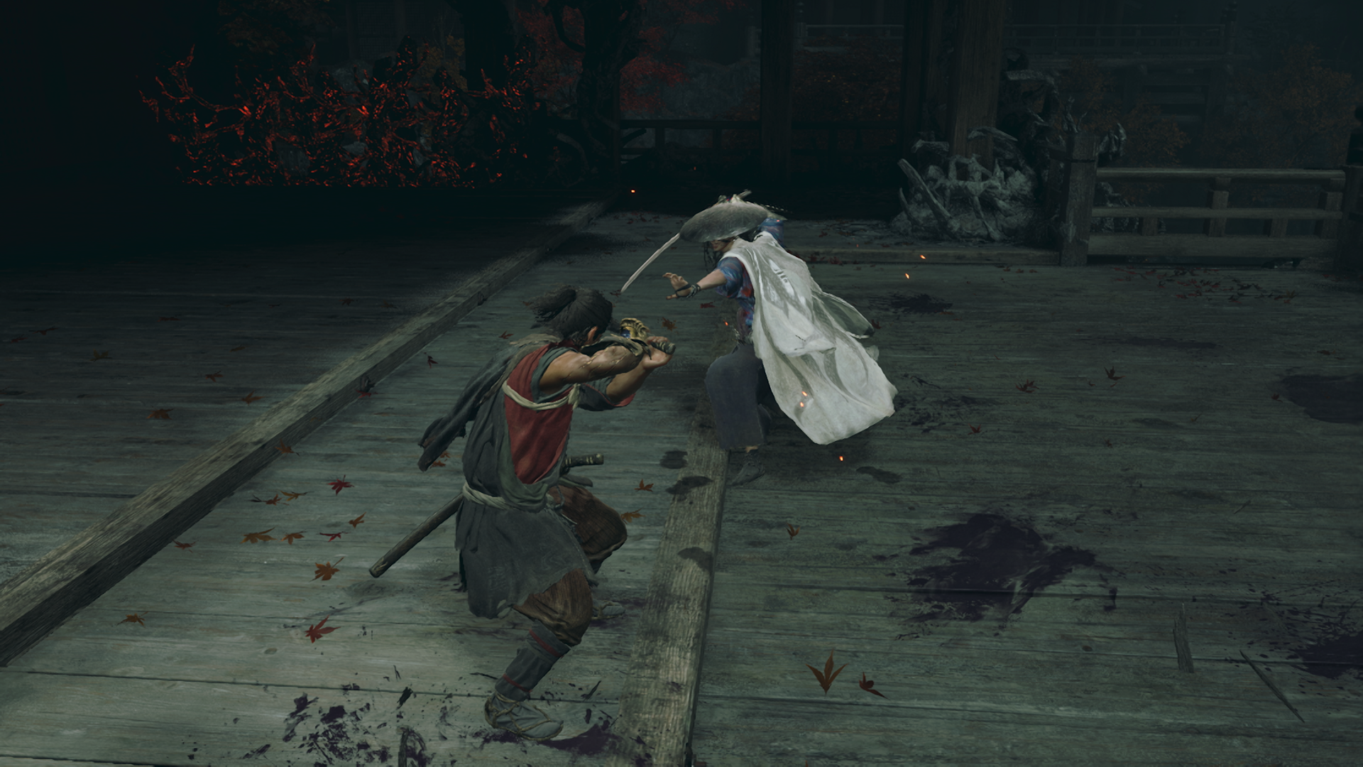 Capture d’écran de Onimusha: Way of the Sword montrant deux samouraïs s’affrontant sur une plateforme en bois sombre, couverte de feuilles rouges et de taches de combat. Le héros, en posture défensive, fait face à un adversaire au manteau blanc et au chapeau de paille, dans une ambiance tendue et cinématique.