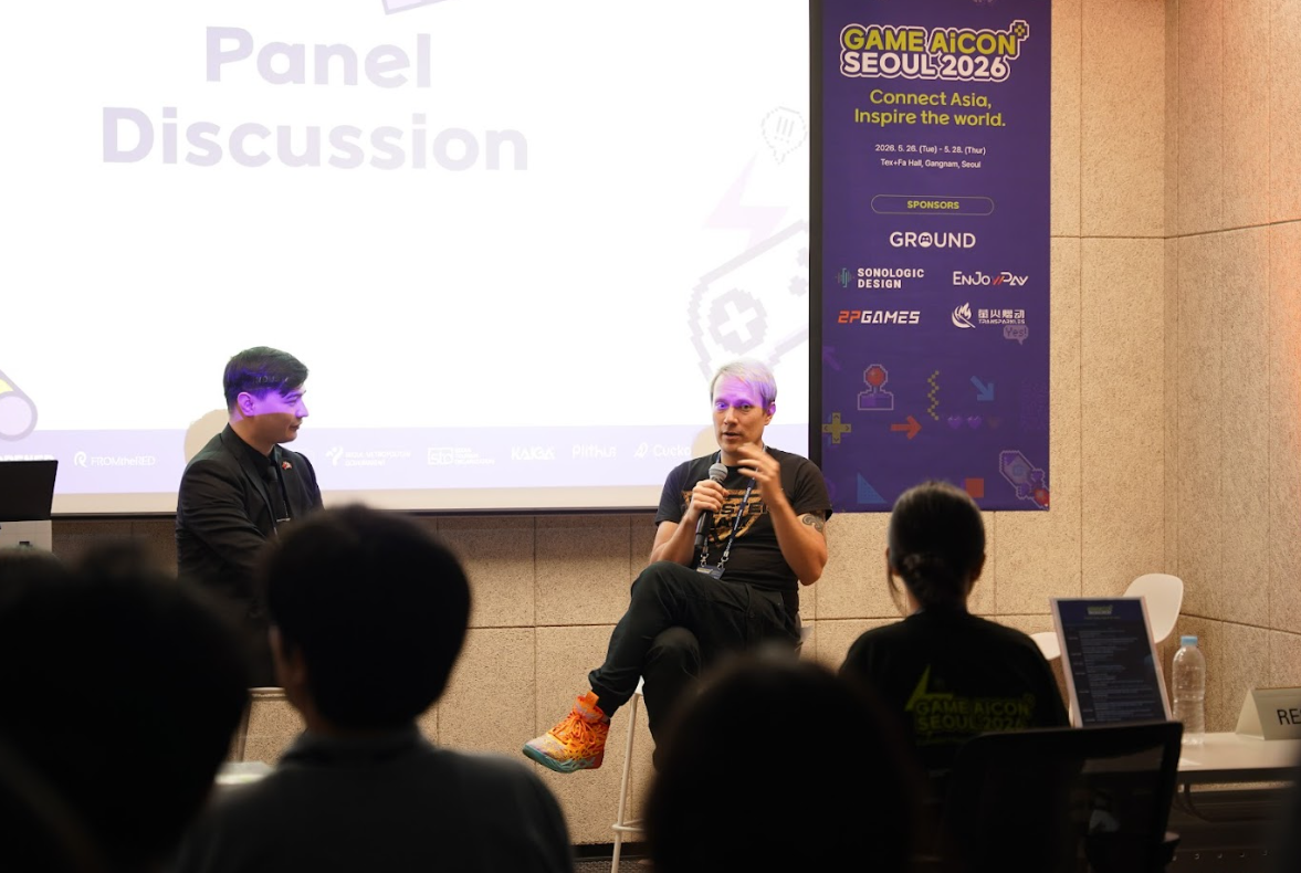 Table ronde au GAME AiCON Seoul 2026 devant un public, avec deux intervenants assis sur scène. Une diapositive affiche « Panel Discussion » et une bannière latérale rappelle le slogan « Connect Asia, Inspire the world » ainsi que les dates de l’événement à Séoul.