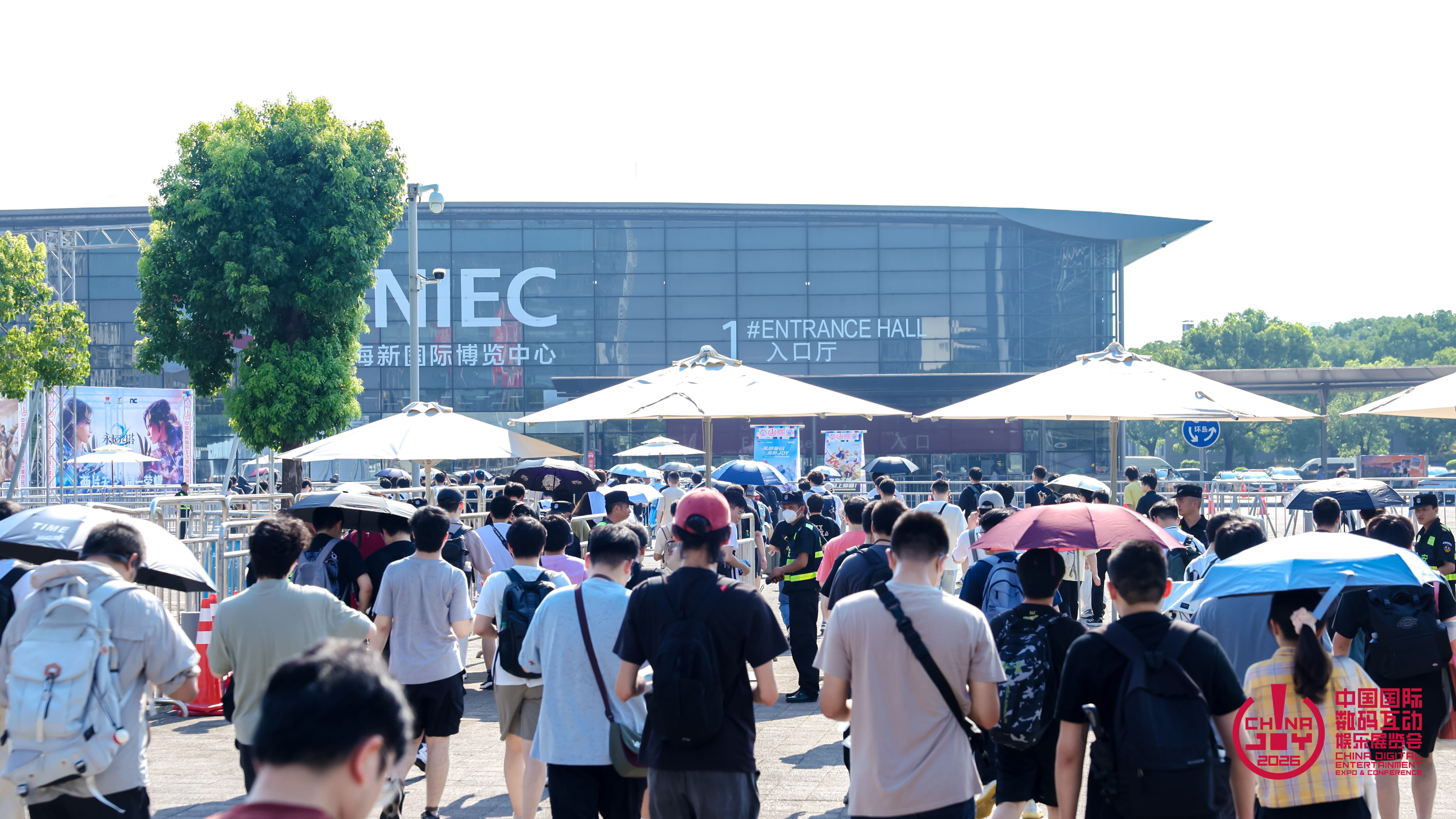 Foule de visiteurs se dirigeant vers l’entrée du Shanghai New International Expo Centre, certains protégés du soleil par des parapluies. Le bâtiment vitré affiche « 1# Entrance Hall », tandis que le logo ChinaJoy 2026 apparaît en bas à droite.