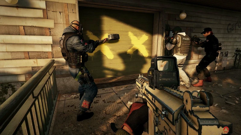Capture d’écran tactique du jeu Tom Clancy’s Rainbow Six Siege, montrant une équipe d’intervention en train de préparer une brèche sur une porte barricadée. La scène se déroule à l’extérieur d’une maison en bois, visiblement délabrée. Au centre, une porte verte marquée de deux grandes croix jaunes signale qu’elle a été renforcée par les défenseurs. Un opérateur lourdement équipé s’approche pour poser une charge explosive, pendant qu’un autre joueur, au premier plan, vise avec un fusil d’assaut beige muni d’un viseur holographique. À droite, deux autres membres de l’escouade en uniforme "POLICE", l’un en blanc et l’autre en noir, s’alignent sur le mur pour couvrir l’entrée, prêts à intervenir dès l’ouverture. Un corps gît au sol, suggérant qu’un échange de tirs a déjà eu lieu. L’environnement est réaliste, avec des textures détaillées, des éclats de bois, et une lumière dorée de fin de journée qui baigne la scène. L’image reflète l’essence du gameplay stratégique de Rainbow Six Siege, centré sur la coopération, la planification minutieuse et les confrontations tendues entre attaquants et défenseurs dans des espaces confinés.