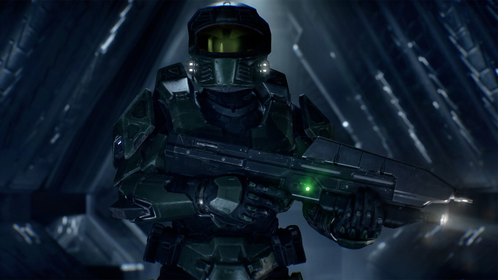 Visuel promotionnel de Halo montrant le Spartan Master Chief en armure verte tenant un fusil d’assaut dans un couloir métallique sombre de vaisseau ou de station spatiale. Son casque à visière dorée et les lumières de son équipement ressortent dans l’éclairage froid, renforçant l’atmosphère de science-fiction et de combat.