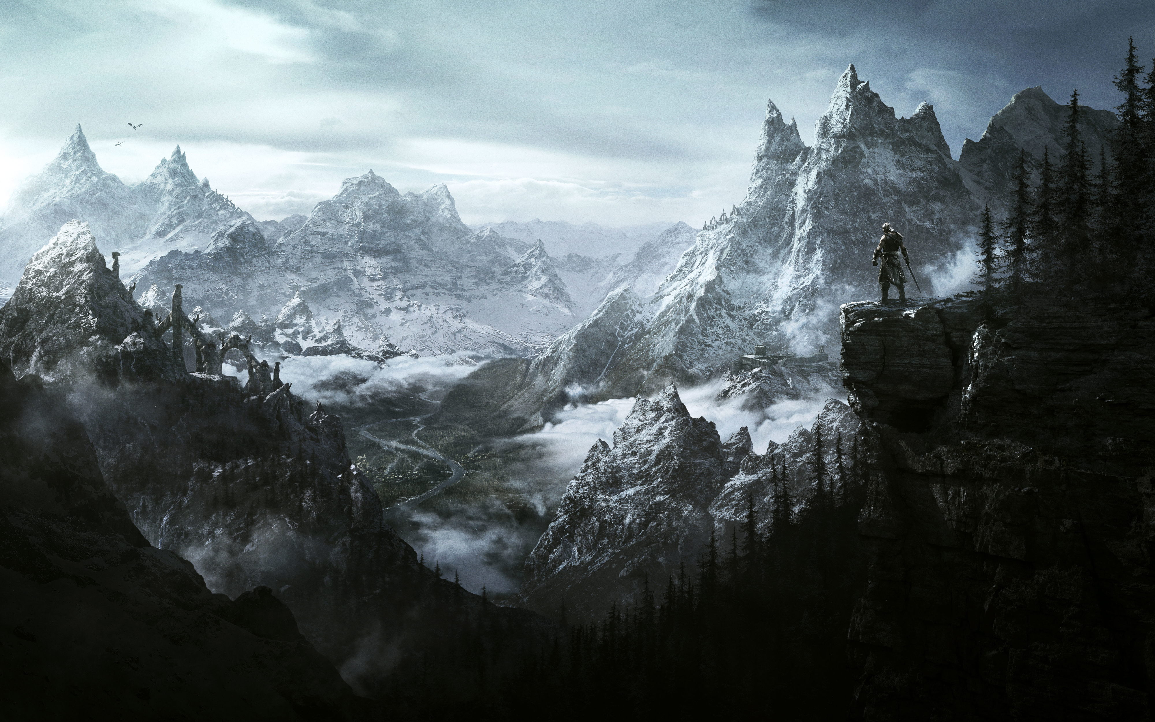 Panorama de Skyrim montrant un aventurier solitaire sur une falaise, face à une vaste chaîne de montagnes enneigées. Une vallée brumeuse, des forêts de conifères et des ruines se déploient sous un ciel gris.