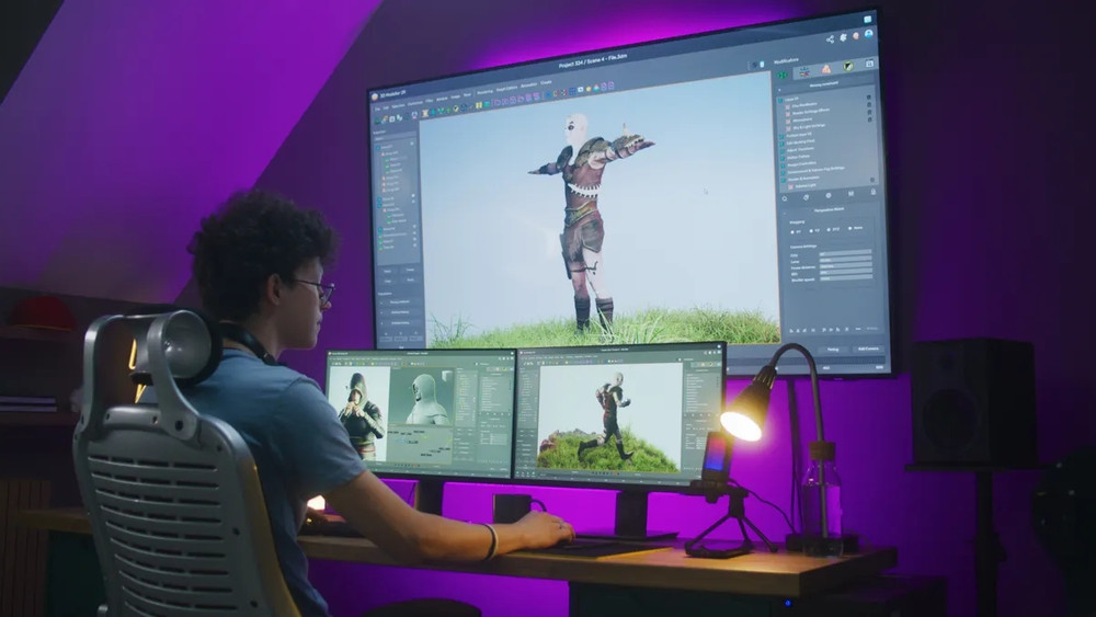Jeune développeur ou artiste 3D assis à son bureau dans une pièce à l’éclairage violet tamisé, travaillant sur un projet de modélisation ou d’animation de personnage pour un jeu vidéo. Il utilise une configuration à trois écrans : deux moniteurs sur le bureau et un grand écran mural au-dessus, tous affichant une interface de logiciel de création 3D. L’écran principal montre un personnage humanoïde en armure de cuir, debout sur une colline herbeuse sous un ciel bleu clair. Les autres écrans affichent différentes vues et détails du même personnage. Le bureau est équipé d’un éclairage directionnel, d’un micro monté sur bras articulé et d’une bouteille d’eau, suggérant un environnement de travail professionnel dédié à la création de contenu vidéoludique.