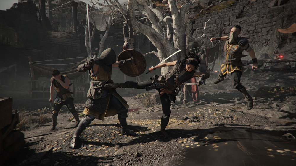 Capture de gameplay d’un jeu d’action fantasy montrant un combat dans des ruines sombres. Un personnage armé d’une épée donne un coup de pied à un garde avec bouclier, tandis que deux autres ennemis s’approchent dans un décor de pierre, d’arbres morts et de terrain boueux.