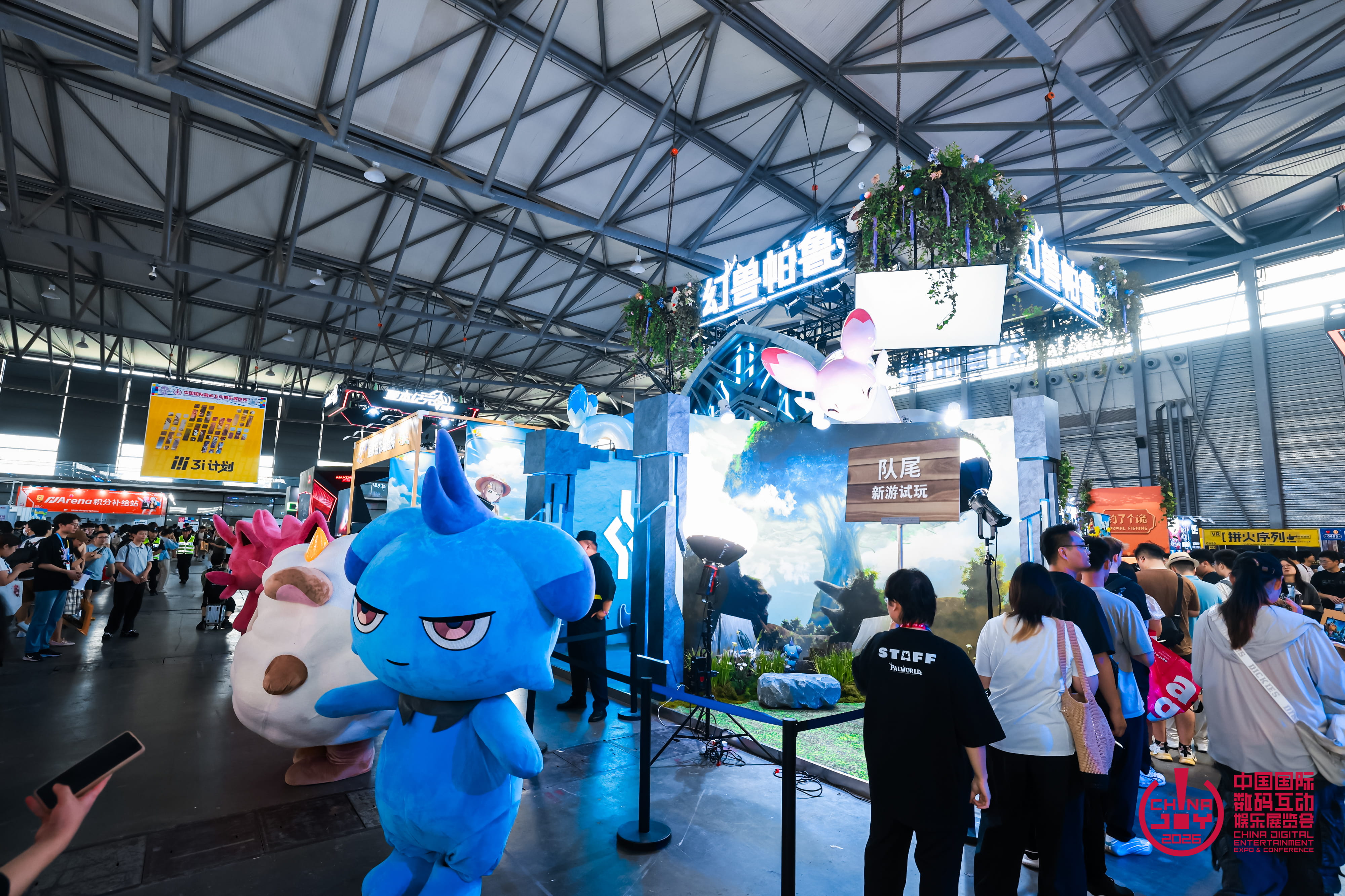 Stand Palworld à ChinaJoy 2026, décoré de végétation et de grands écrans, avec plusieurs mascottes colorées du jeu, dont une créature bleue au premier plan. Des visiteurs font la queue autour du stand tandis qu’un membre du personnel portant un t-shirt Palworld se tient à proximité.