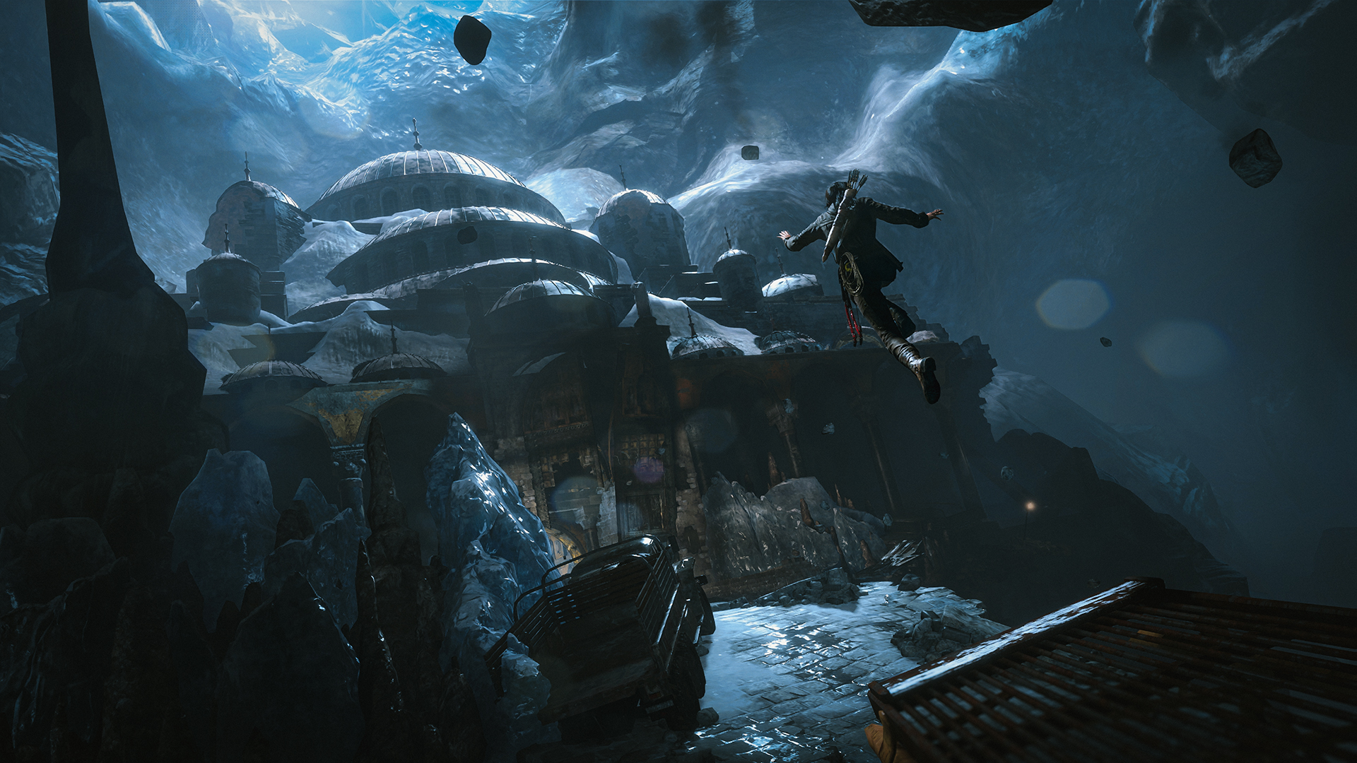 Capture d’écran de Rise of the Tomb Raider montrant Lara Croft sautant au-dessus de ruines glacées dans une immense caverne bleutée. Elle se dirige vers un ancien bâtiment à coupoles, entouré de glace, de rochers flottants et d’une lumière froide, dans une scène d’exploration périlleuse et spectaculaire.
