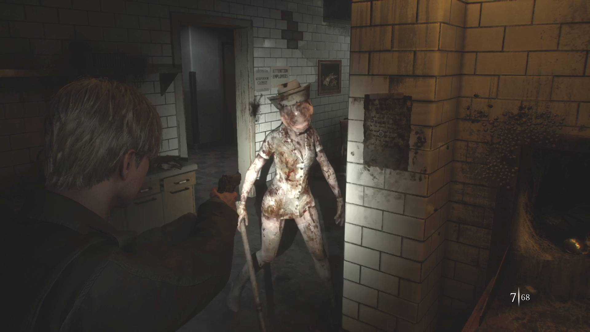Capture d’écran angoissante issue du remake de Silent Hill 2, représentant une confrontation tendue entre le protagoniste James Sunderland et une créature cauchemardesque dans un environnement hospitalier délabré. À gauche, James, visible de dos, pointe son arme de poing vers une infirmière monstrueuse, emblématique de la série, qui s’approche lentement de lui. La créature a une apparence humanoïde féminine mais grotesque : sa tête est déformée et sans traits distincts, recouverte d’un bonnet d’infirmière taché, tandis que sa tenue blanche moulante, maculée de sang, accentue la déformation de son corps. Elle tient un objet contondant dans sa main droite, prêt à frapper. La pièce est carrelée de murs blancs souillés, éclairée par une lumière chaude et trouble, avec des détails sinistres comme des moisissures et une ouverture sombre remplie de toiles au fond à droite. L’ambiance est pesante, oppressante et propre à l’horreur psychologique de Silent Hill, où les ennemis reflètent les traumatismes intérieurs du héros. Le chiffre "7 | 68" en bas à droite de l’écran indique les balles restantes, soulignant l’urgence et la gestion de ressources propre au gameplay du survival horror.