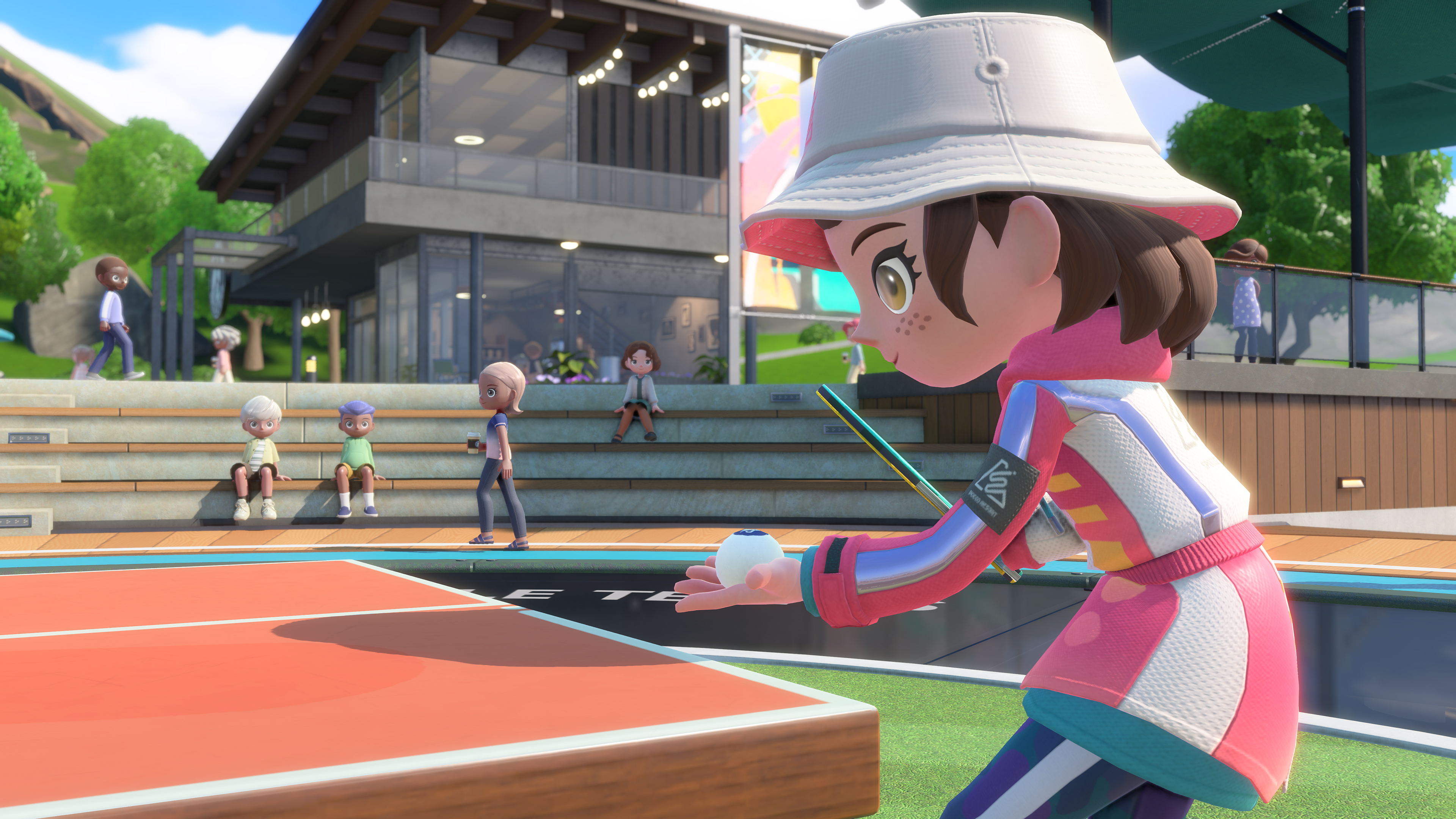 Capture d’écran de Nintendo Switch Sports Resort montrant un personnage en tenue rose prêt à servir au tennis de table, raquette à la main et balle posée dans la paume. La scène se déroule en extérieur, sur un terrain ensoleillé entouré de spectateurs et de bâtiments modernes à l’ambiance détendue.