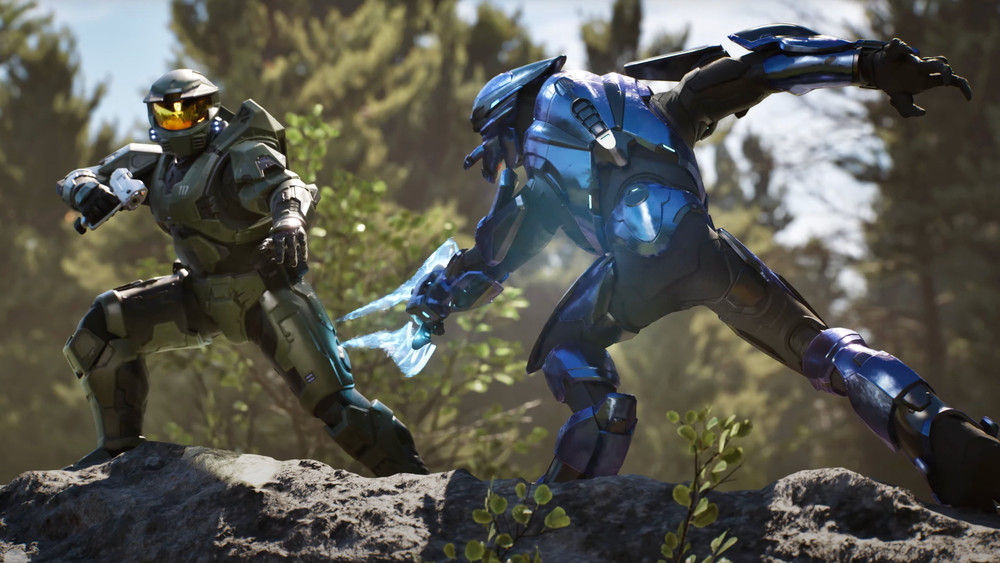 Capture de jeu Halo montrant deux combattants en armure s’affrontant sur un terrain rocheux en forêt : un Spartan vert se tient sur la gauche tandis qu’un adversaire en armure bleue bondit vers lui avec une arme énergétique.