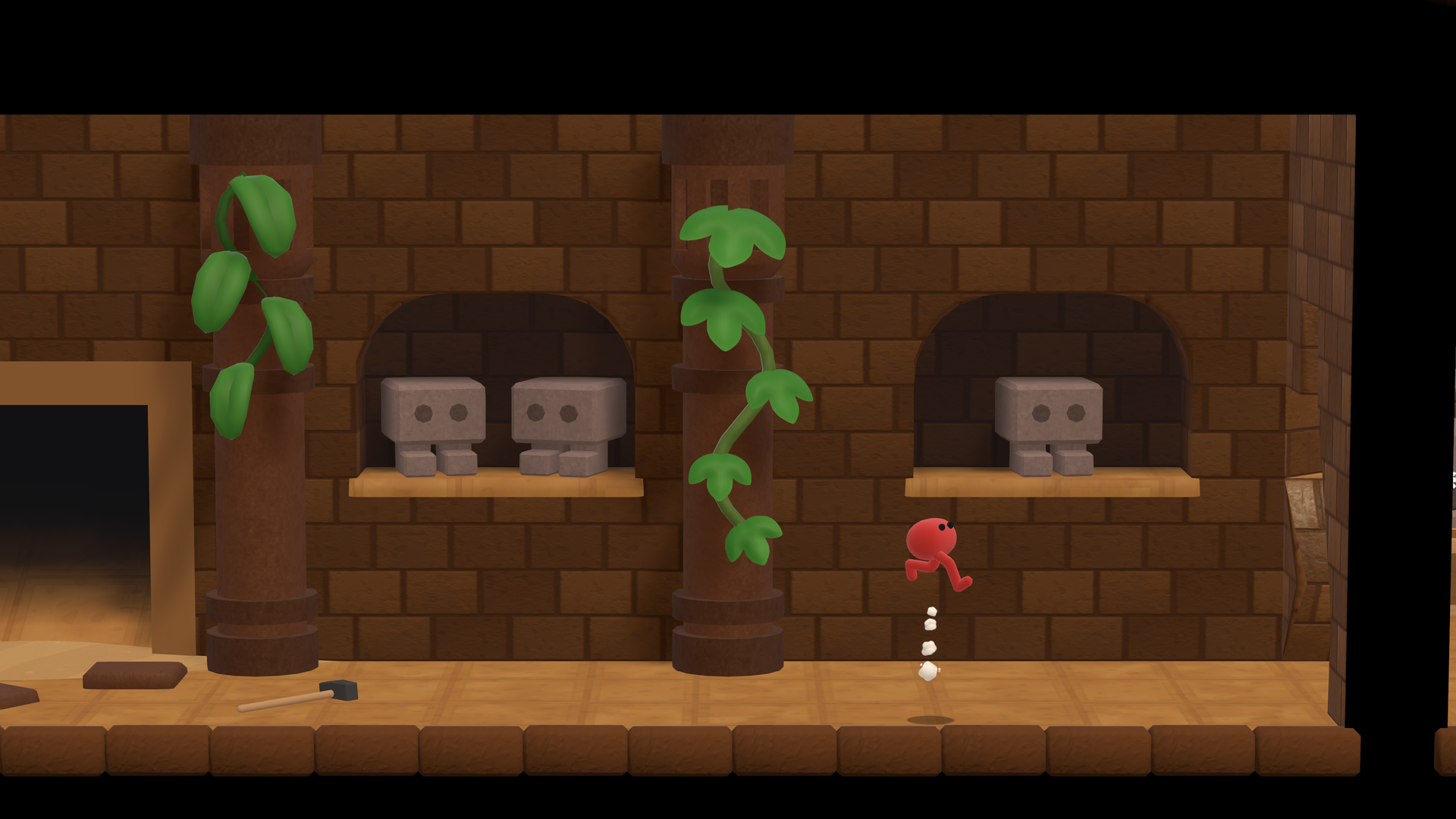 Capture d’écran de Pikuniku 2 montrant un petit personnage rouge qui saute dans un décor de plateforme en briques, avec des colonnes couvertes de lianes vertes. Des blocs de pierre aux yeux ronds sont posés dans des niches, tandis qu’un marteau au sol et les passages sombres renforcent l’ambiance de puzzle-aventure simple et amusante.