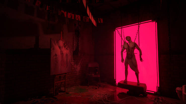 Capture d’un jeu d’horreur montrant une pièce obscure baignée de lumière rouge, avec une grande créature humanoïde suspendue par des chaînes devant un panneau rectangulaire rose vif.
