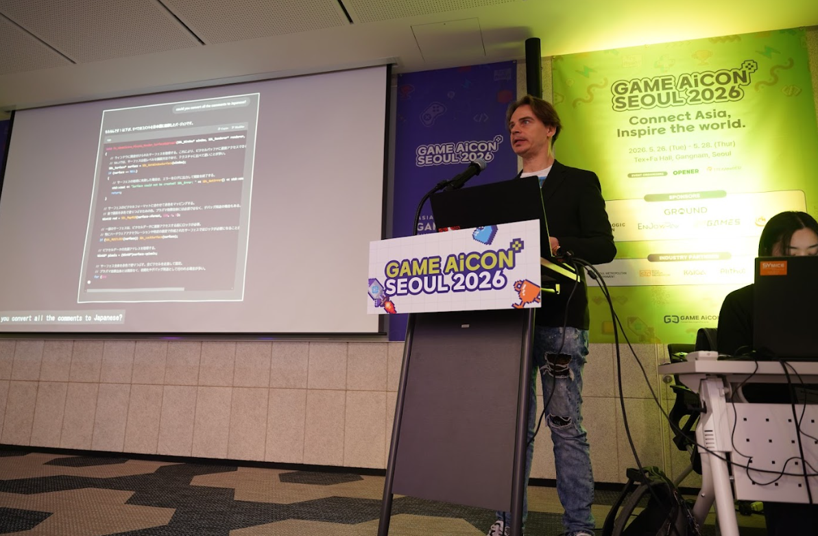 Conférencier au pupitre GAME AiCON Seoul 2026 lors d’une présentation sur l’IA et le jeu vidéo. Une diapositive avec du code et du texte en japonais est projetée à gauche, tandis qu’une affiche verte rappelle le slogan « Connect Asia, Inspire the world » et les dates de l’événement à Séoul.