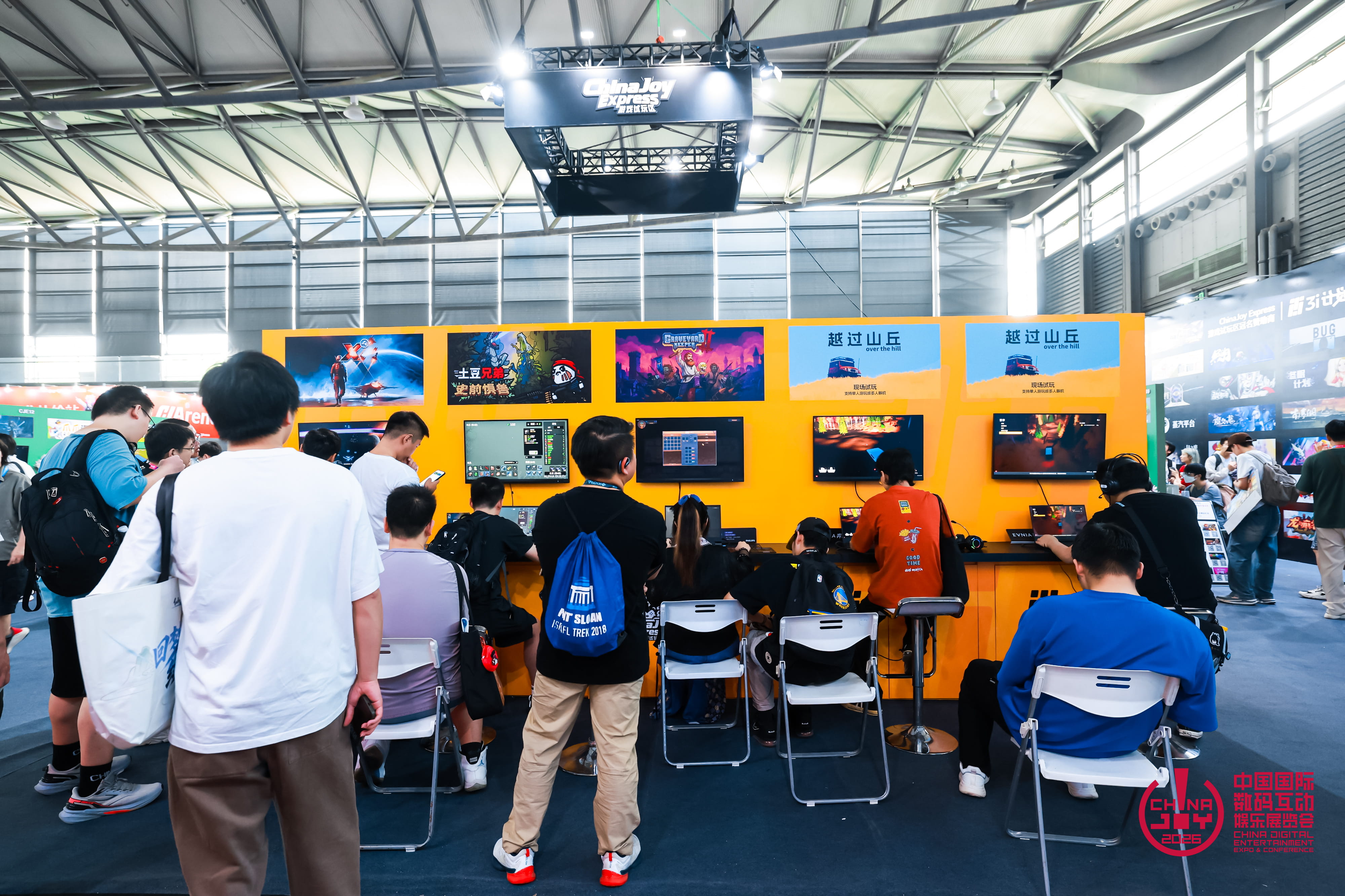 Espace de démonstration ChinaJoy Express à ChinaJoy 2026, où plusieurs visiteurs testent des jeux sur ordinateurs portables face à un mur orange équipé d’écrans. D’autres participants observent les parties dans cette zone dédiée notamment aux jeux indépendants.
