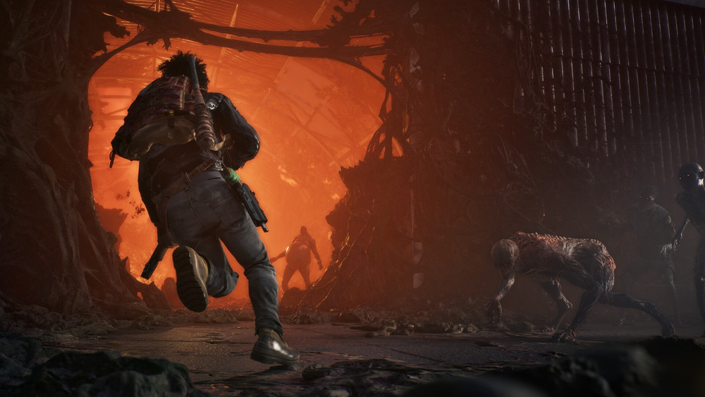 Capture de jeu montrant un personnage armé courant dans un environnement industriel en ruines, éclairé par une intense lueur orange. Plusieurs créatures humanoïdes menaçantes se tiennent dans l’obscurité autour de lui.