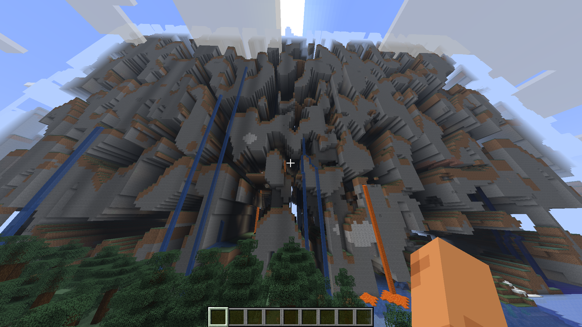 Capture de Minecraft en vue à la première personne montrant un terrain montagneux fortement déformé, composé d’immenses falaises et cavités de pierre. Plusieurs cascades et coulées de lave descendent jusqu’à une forêt, tandis que des fragments de terrain semblent flotter dans le ciel.